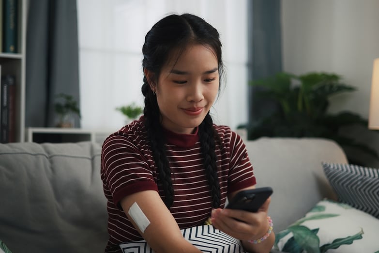 woman on her phone with a glucose monitor on her arm