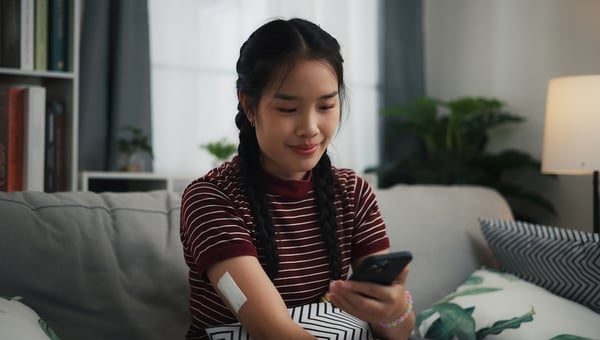 woman on her phone with glucose monitor on her arm